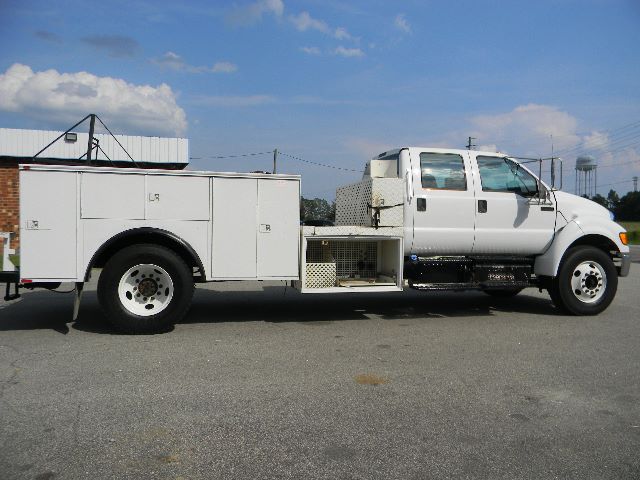 Service/Utility truck side view showing utility compartments, Cranked exhaust, and crew cab; white Ford F-750 with utility bed and ladder rack.