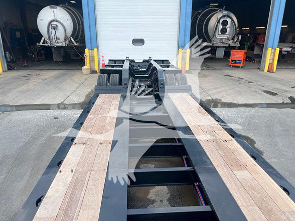 XL Specialized XL110Hdgs18 lowboy trailer deck with wood planks and gooseneck hitch visible; background shows service bays and equipment.