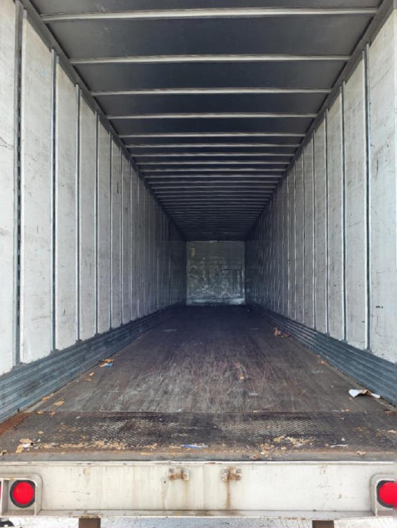 Trailer interior showing empty cargo space with metal side walls and ceiling, wooden floor, rear open tailgate, and taillights visible at bottom corners.
