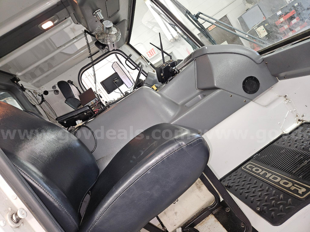 Truck cab interior of a 2003 Sterling M-B paint marker truck showing driver seat, steering column, dashboard, and floor mat with 'CONNOR' branding; visible gray panels and control levers.