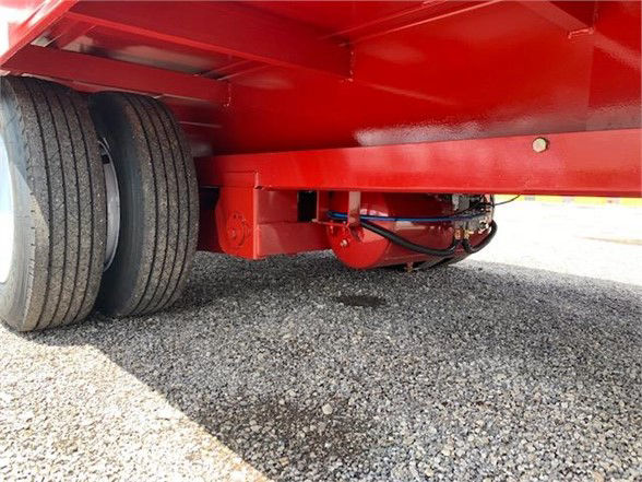 Rear view of a red drop deck trailer showing dual rear wheels and undercarriage with hydraulic lines.