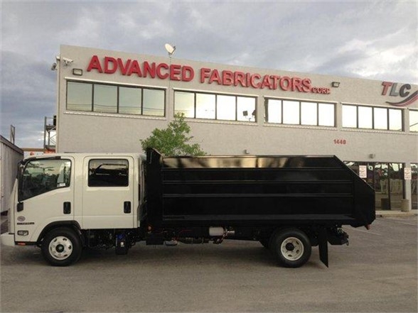 Dump truck with a black dump body in front of a beige building that reads ADVANCED FABRICATORS. Stock number 14LD48S visible; side view shows white cab and black dump body.