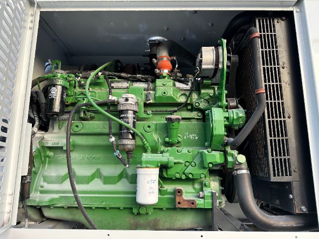 Green diesel engine in industrial truck compartment with radiator on right and hoses connected; visible filters and belts.