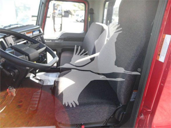 Truck cabin interior of a 2024 Mack MD6 showing steering wheel, driver seat, and dashboard with red exterior visible.
