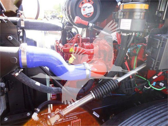 Truck engine bay visible with hoses, blue coolant hose, red components, and various wiring and clamps.