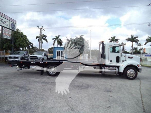 Peterbilt 337 tow truck side view with flatbed, stock number visible in background, palm trees, dealership lot.