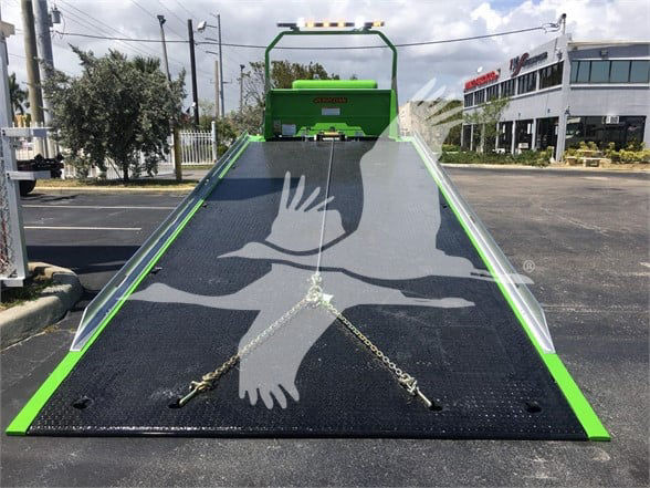 Peterbilt 337 flatbed tow truck in green with hydraulic ramp surface and safety rails, front view.