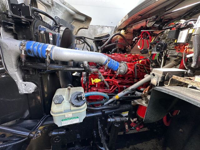 Truck engine bay of a 2014 Freightliner 114SD showing red engine block, blue coolant hose, black radiator, white/green coolant reservoir, exposed wiring, and various hoses.