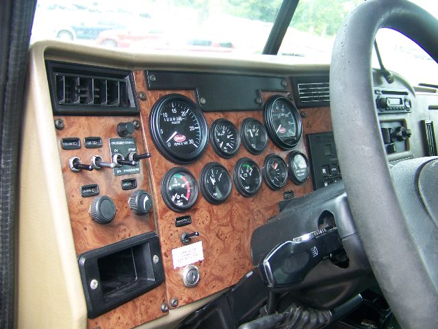 Peterbilt truck dashboard with wood grain panel and multiple gauges, steering wheel on right, various switches and knobs visible.