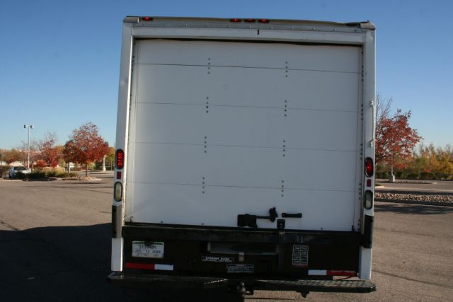 Rear view of a white cargo box truck with a large rear roll-up door and taillights on both sides; some small decals and a license plate area on the bumper.