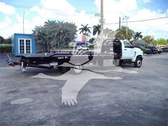 Tow truck with flatbed trailer attached to a white International CV truck. The image shows the cab and long black flatbed, with a watermark of a crow image across the center.