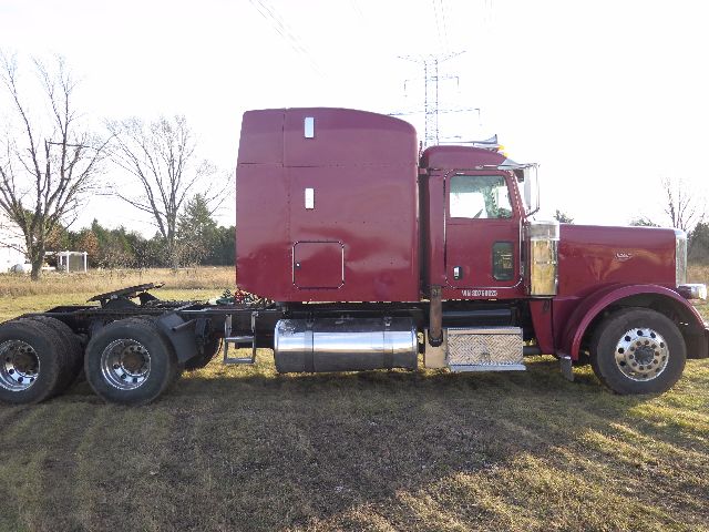 Peterbilt 388 semi truck in red with sleeper cab, side view showing fuel tanks, chrome exhaust, and dual rear axles.