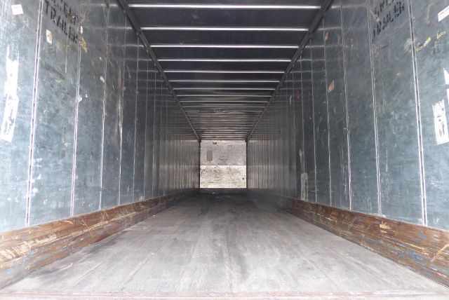 Interior of a trailer cargo area with metal walls and wooden scuffed base showing a long empty space.