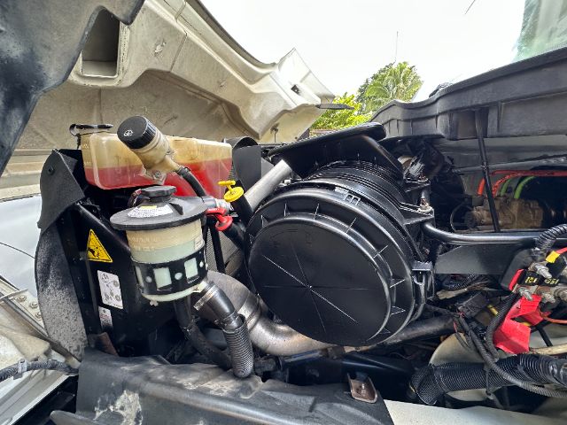 Engine bay of a 2009 International 7500 vacuum truck showing air filter housing, coolant reservoir, and various hoses.