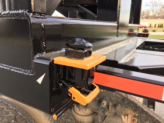 Close-up of trailer hitch and orange safety latches on a black 2003 Wabash tipper trailer chassis, showing part of the suspension and frame.