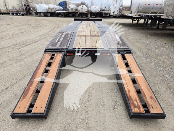 Flatbed trailer deck with wooden planks and metal side rails, long perspective view at a truck yard.