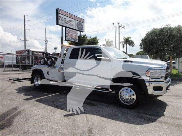 2024 Ram 5500 SLT truck in white viewed from a side angle showing long cab, flatbed, chrome wheels, and dealership lot in background; watermark of a hand/dove logo overlays image.