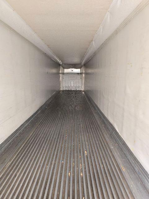 Interior of a long empty trailer with ribbed floor and white walls, rear door visible at far end.