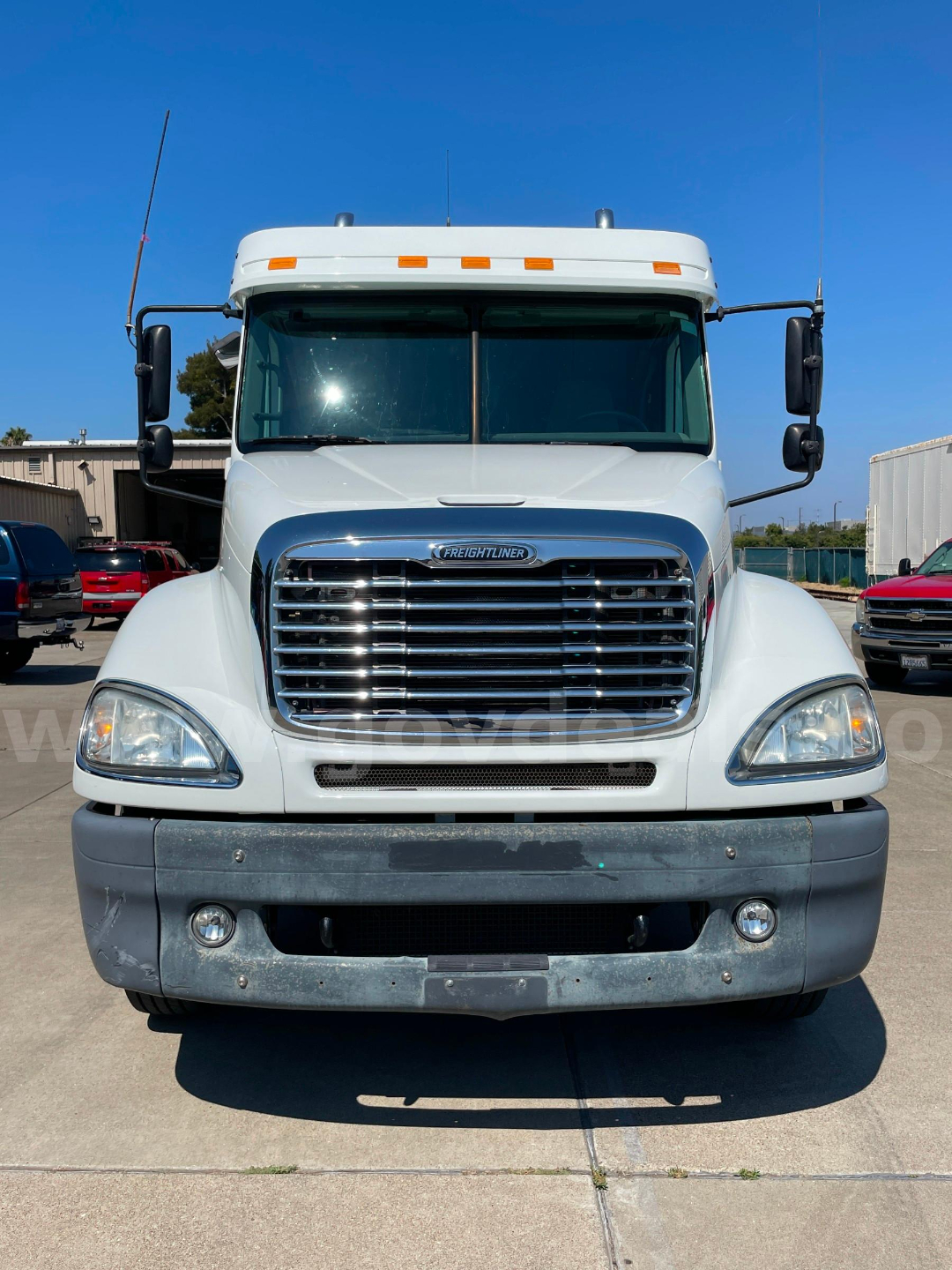 Freightliner cab and chassis front view showing chrome grille, headlights, and white hood with cab, with bumper and tall mirrors on both sides.