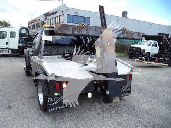 Tow truck with flatbed and hook attachment viewed from rear quarter, Ford F-450 in-service with light bar and rear lights visible.