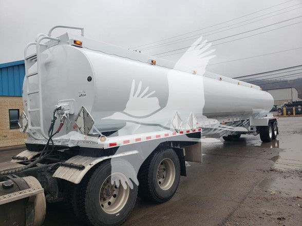 Tank trailer in a light gray color with a long cylindrical tanker, rear dual wheels, ladders and hoses at the front left. Small text on the front end near the connection points.