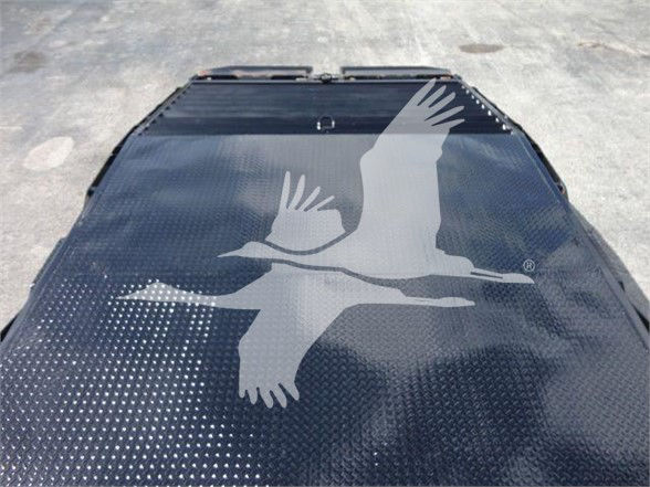 Vehicle flatbed or trailer deck with textured black surface and a white logo of a flying bird. No other readable text visible.