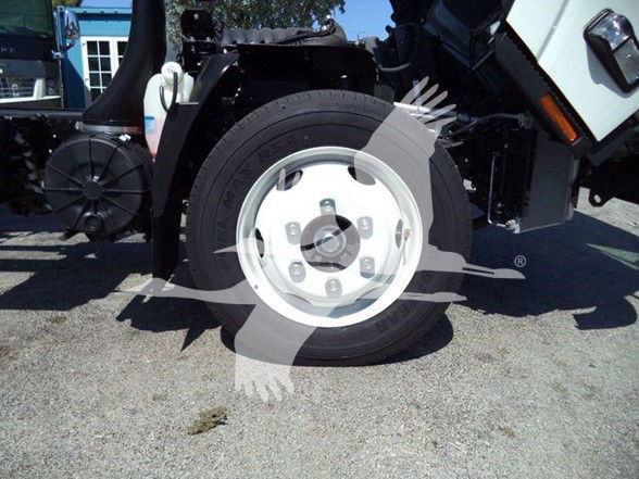 Isuzu NPR HD wheel and front section showing wheel, lug nuts, and part of suspension in a truck yard.