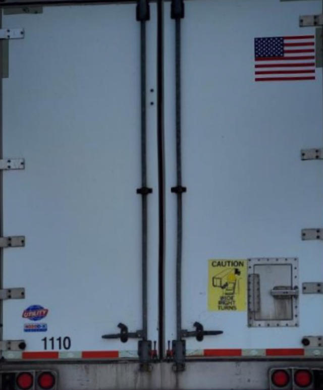 Rear view of a white utility trailer with double doors, American flag sticker, yellow caution label, and number 1110.