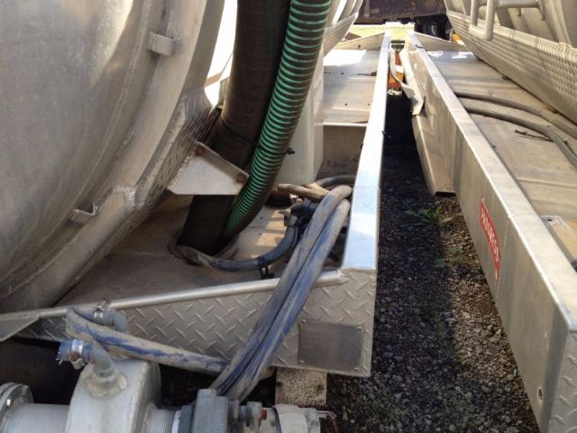 Truck trailer or vacuum tank connection area showing hoses, cables, metal frame, and diamond plate steps.