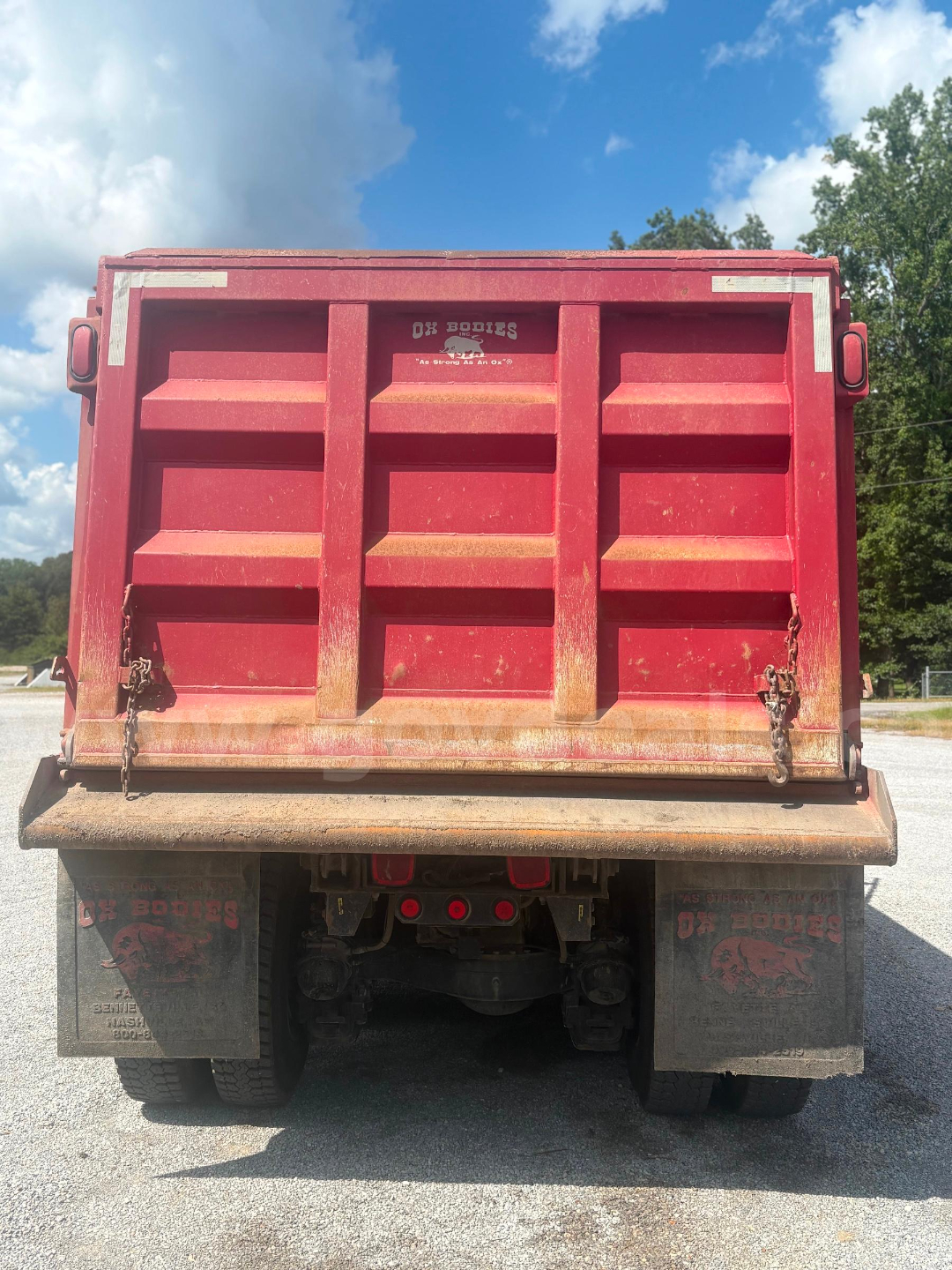 Rear view of a red dump truck bed with two black mud flaps and chains, showing 'OK Bodies' branding on the tailgate.