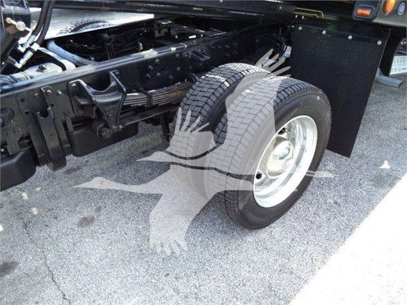 Truck rear-left wheel area showing spare wheel and chassis components; visible large front tire, white steel wheel, black chassis rails, and utility panels.