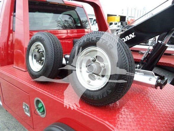 Ram 4500 tow truck bed with two spare tires on diamond plate surface and hydraulic equipment in background.