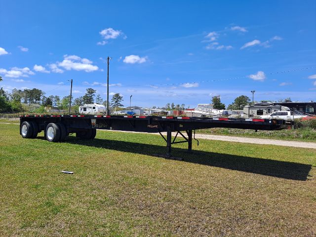 Flatbed trailer with dual rear axles and a long black frame, unused-looking air dam, set on grass under blue sky.
