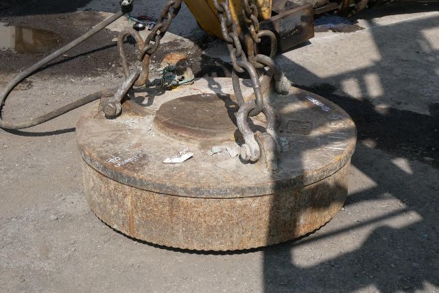 Heavy circular magnet weight with chains attached, rusted surface, industrial equipment in a yard.