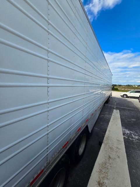 Long white Great Dane trailer side with ribbed metal siding and tires visible at rear, parked in lot under blue sky.