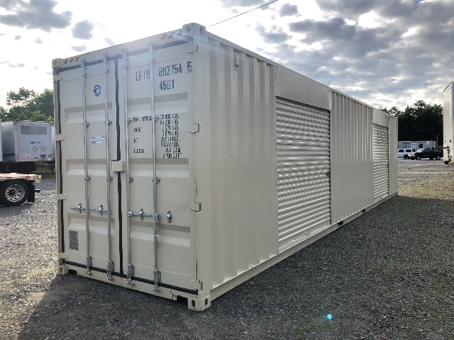Long beige shipping container trailer with vertical corrugated walls and double doors at rear, set on a gravel lot under a cloudy sky.