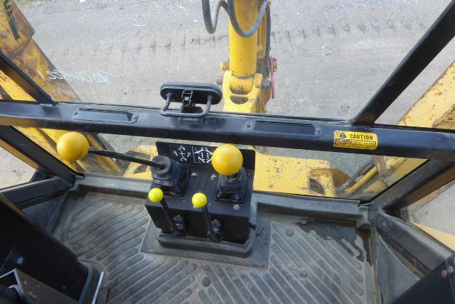 Cab controls inside Massey Ferguson 50HX backhoe cab showing joysticks and yellow knobs, floor mat, and window frame.