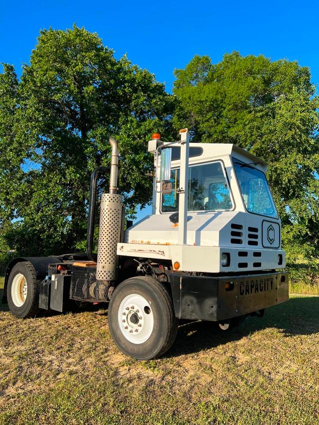 Truck tractor Cab interior visible with large exhaust stack and front grille, white color, black bumper, rear wheel and chassis shown.
