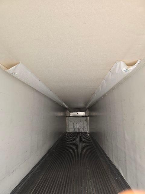 Interior of a refrigerated trailer with white walls and ribbed floor, empty long box with ceiling hatch at far end.