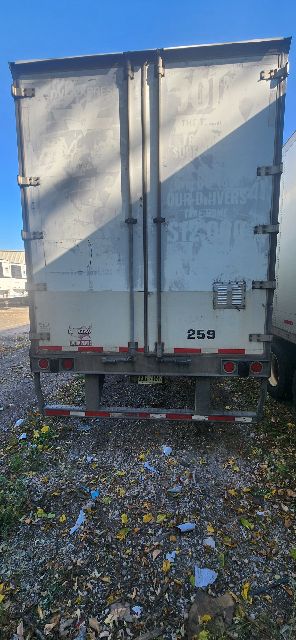 Rear view of a white Wabash dry van trailer with doors closed; visible markings include a serial sticker and some text on the door.
