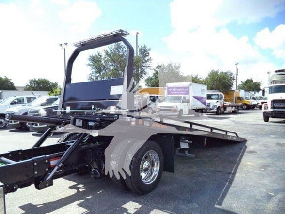 Tow truck flatbed chassis with wheel and hydraulic ramp, International MV style, stock image background.