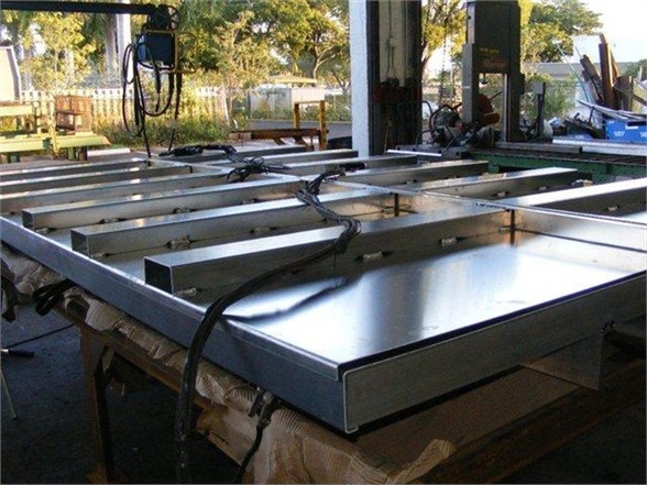A flat metal dump body frame or platform on a workbench, showing welded rails and side panels.
