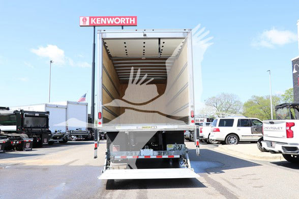 Rear view of a new 2025 Hino L6 cab and chassis with an open cargo box, stock HI1849, Kenworth dealership lot, other trucks visible.