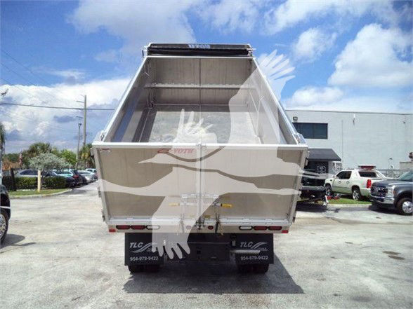 Rear view of a Ford F-550 dump truck with empty dump bed, tail lights, and bumper, in a dealership lot.