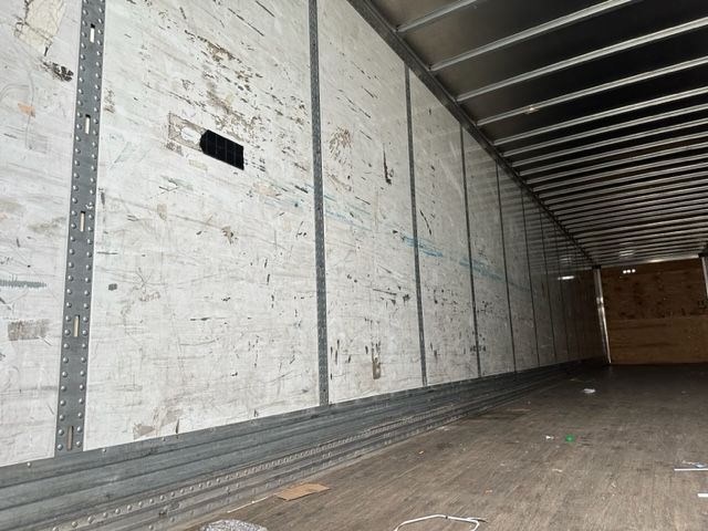 Interior of a 2007 Stoughton dry van trailer showing plywood walls, metal studs, ribbed panels, and a wooden floor with some debris.