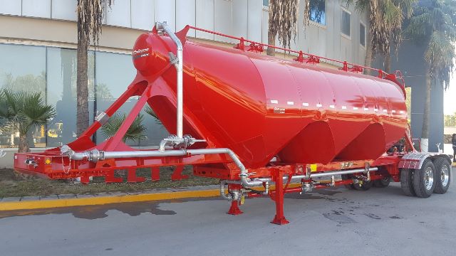 Pneumatic dry bulk trailer in red on a trailer chassis with dual axles and piping along the underside.