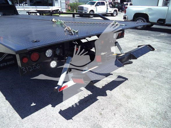 Flatbed tow truck with hydraulic winch area visible, rear lights and chain hooks on diamond plate bed; hitch and ramp visible under platform.