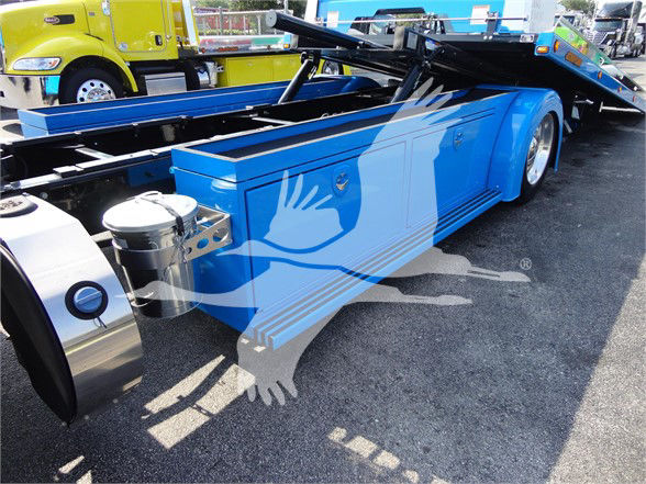 Peterbilt 337 tow truck chassis with blue cab and bed, side tank, and hydraulic wheel lift. Visible text includes 'Peterbilt' on a badge and various components like fuel tank and ladders but no legible model numbers in this view.
