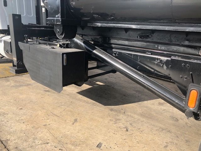 Grapple truck undercarriage showing metal toolbox and hydraulic arm linkage beneath Freightliner M2-112.