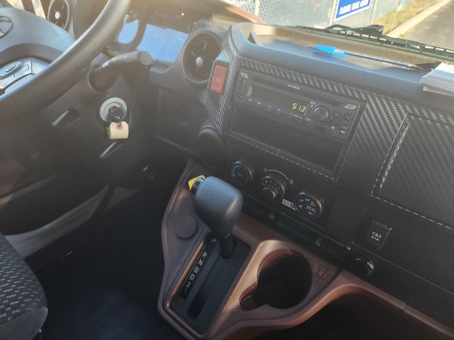 Vehicle interior of a 2025 Hino L6 cab showing steering wheel, ignition key, dashboard with radio, climate controls, gear shifter, and cup holders.